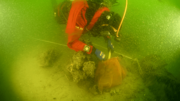 Duikers van de Rijksdienst voor Cultureel Erfgoed inspecteren het afgedekte scheepswrak, foto: NTR